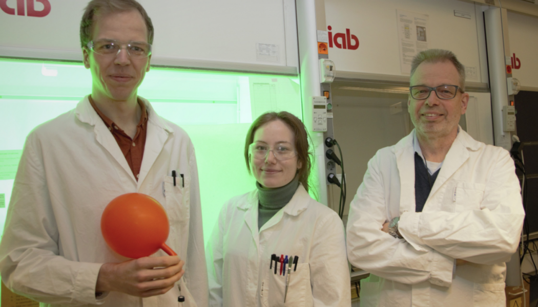 Jesper Schwarz, Aleksandra Ilic och Kenneth Wärnmark visar upp sitt röda järnkomplex inuti en vätgasballong framför en ljusreaktor. På bilden saknas Reiner Lomoth och Catherine Johnson från Uppsala universitet. Foto: Johan Joelsson
